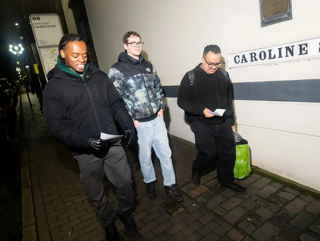 A-group-of-three-people-walking-along-Caroline-Street-at-night-holding-papers-possibly-during-Season-2-Session-1-Mental-Health