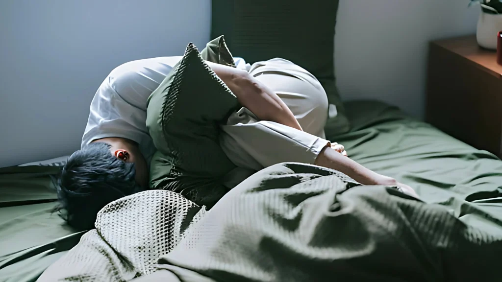 a-person-curled-up-on-a-bed-surrounded-by-green-bedding-their-posture-and-the-muted-lighting-create-a-somber-mood-which-might-be-associated-with-Seasonal-Affective-Disorder