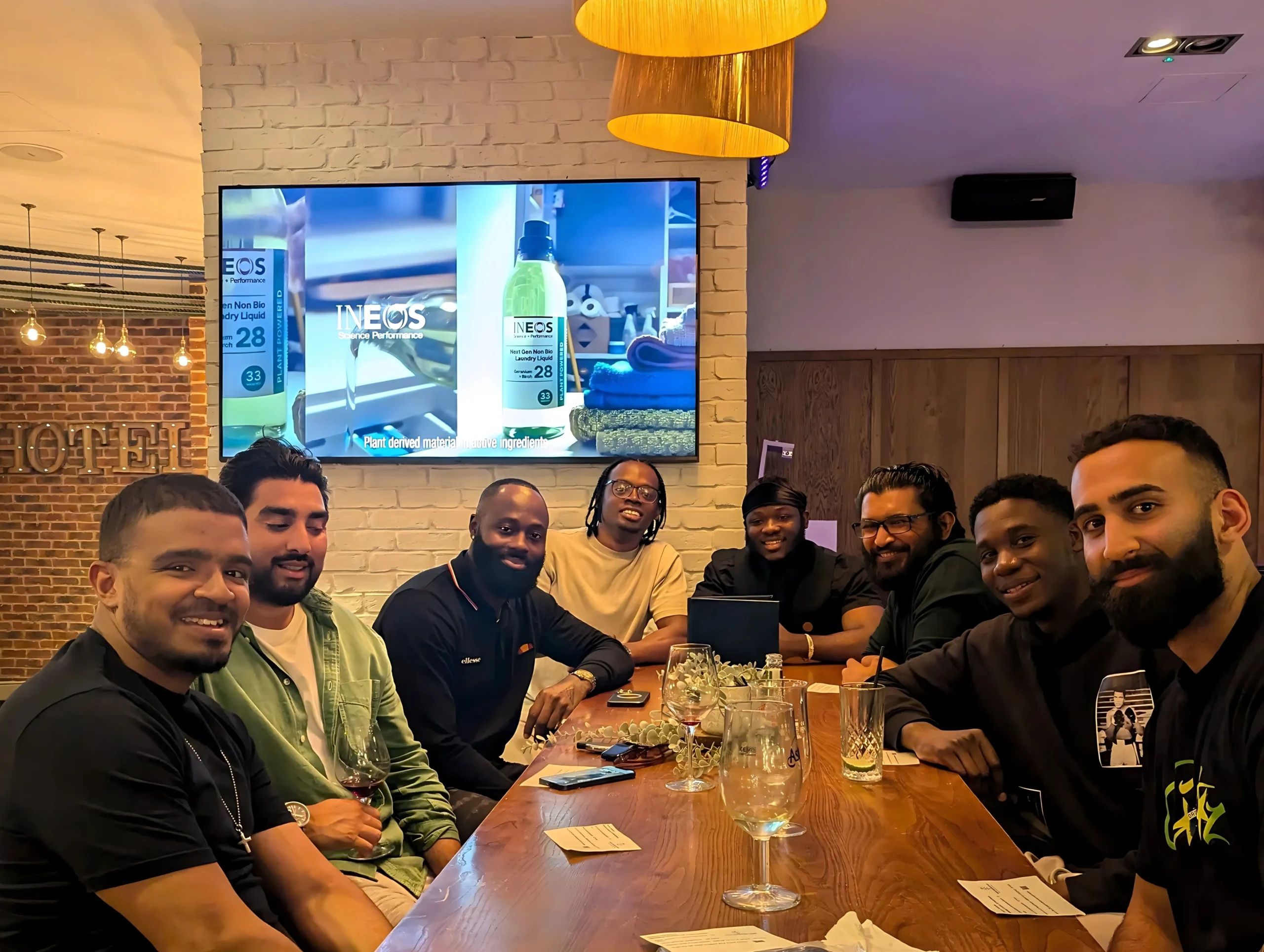 A-group-of-people-enjoying-a-meal-at-a-table-in-a-restaurant-with-a-TV-screen-in-the-background