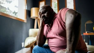 A-distressed-man-sits-with-his-head-in-his-hand-in-a-dimly-lit-room-visually-representing-the-question-How-Does-Mental-Health-Impact-On-Physical-Health