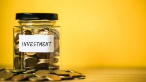 Glass-jar-labeled-Investment-filled-with-coins-on-yellow-background-symbolizing-Prosperity-Wealth