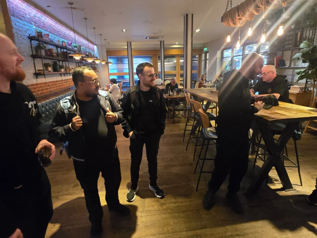 A-group-of-men-chatting-and-standing-in-a-restaurant,-with-one-person-looking-at-the-floor-while-others-are-engaged-in-conversation