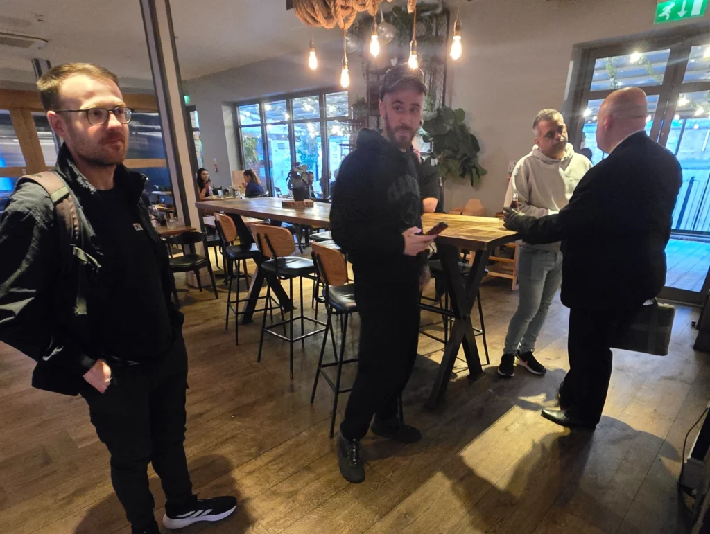 A-group-of-men-sitting-and-standing-in-a-casual-setting,-with-one-person-engaged-in-conversation-with-another-while-others-look-on