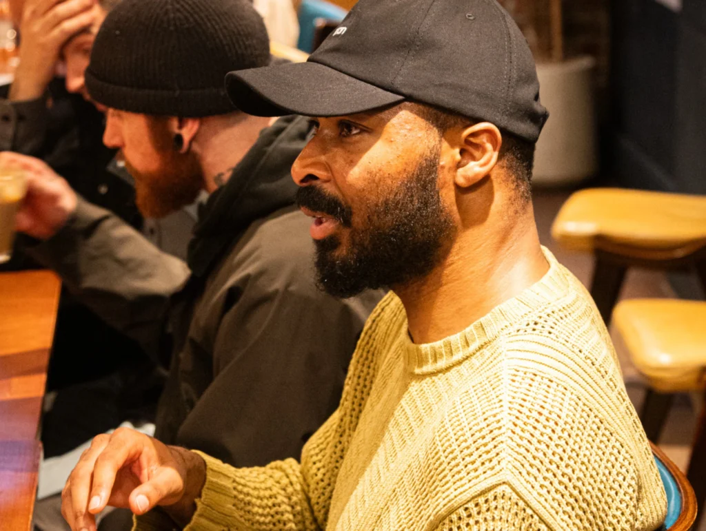 A-man-in-a-yellow-sweater-and-black-cap-talking-with-another-person-in-a-Health-&-Fitness-setting-1