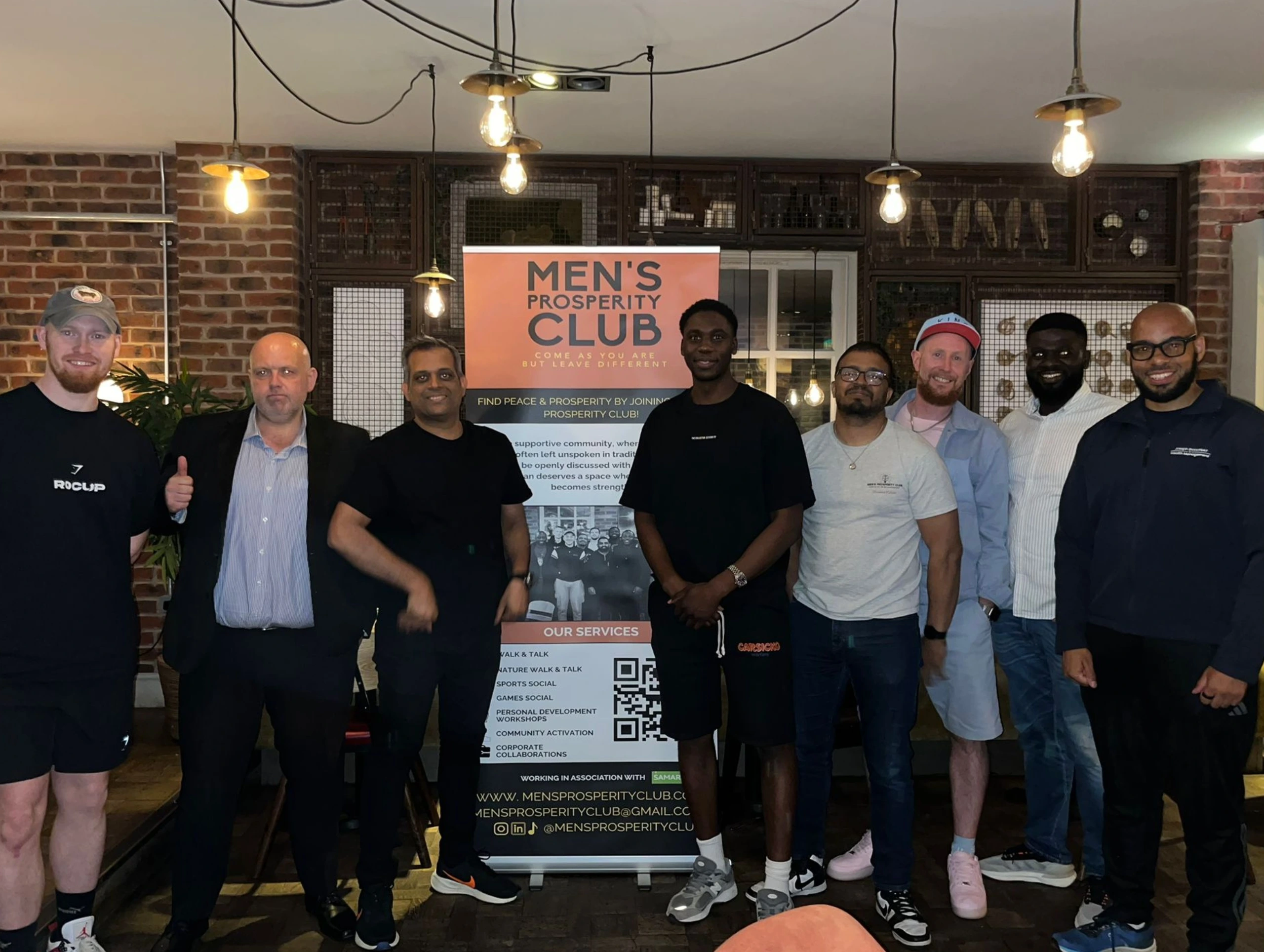 Group-photo-of-Mens-Prosperity-Club-members-with-a-banner-and-the-logo-in-the-background.