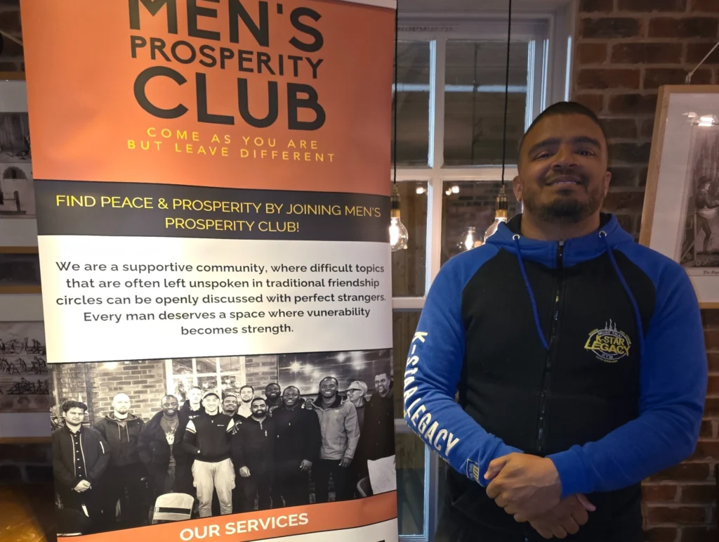 Man-posing-in-front-of-the-Men's-Prosperity-Club-banner-with-a-confident-smile-and-arms-crossed