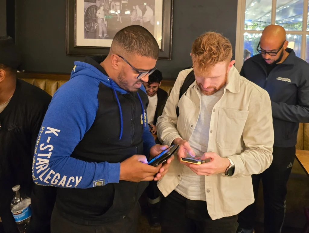 Two-men-looking-at-their-phones,-with-other-men-in-the-background-at-the-event
