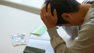 A-man-with-his-hands-on-his-head-feeling-stressed-and-anxious-with-money-and-a-phone-on-the-table
