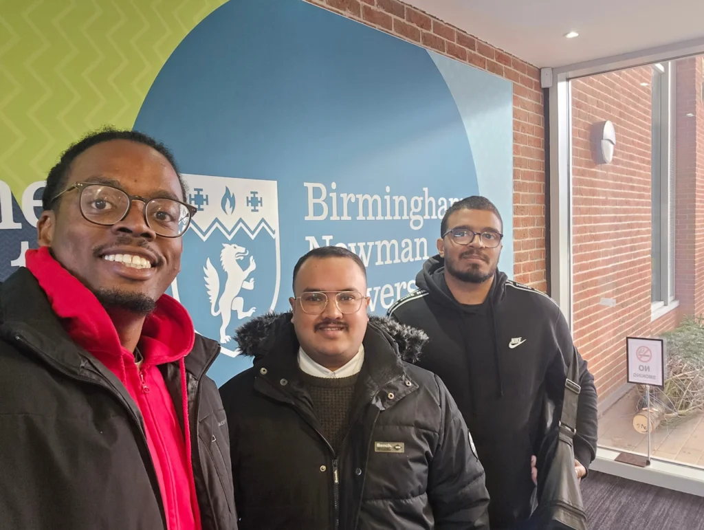 Newman-University-Event-Group-photo-with-attendees-at-the-Men's-Prosperity-Club-booth-in-front-of-the-Birmingham-Newman-University-sign