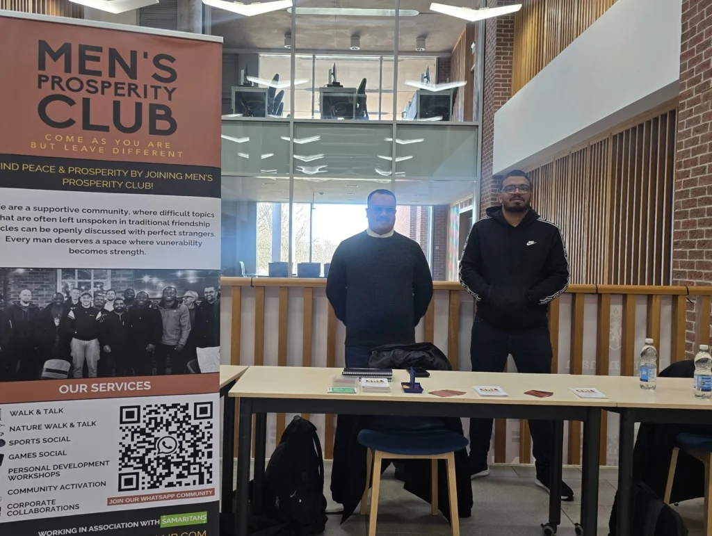 Newman-University-Event-Men's-Prosperity-Club-booth-with-two-participants-standing-beside-the-banner