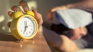 Person-hitting-snooze-button-on-alarm-clock-to-procrastinate